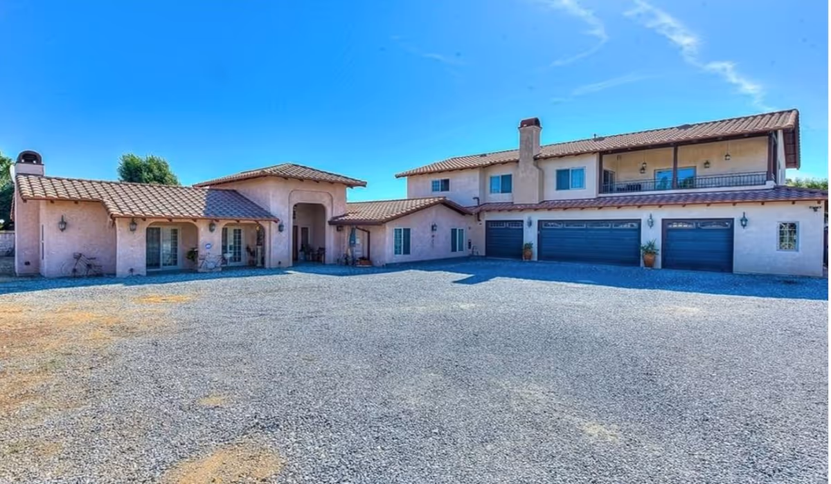 Two-story hacienda-style senior living building with garages and a gravel driveway.