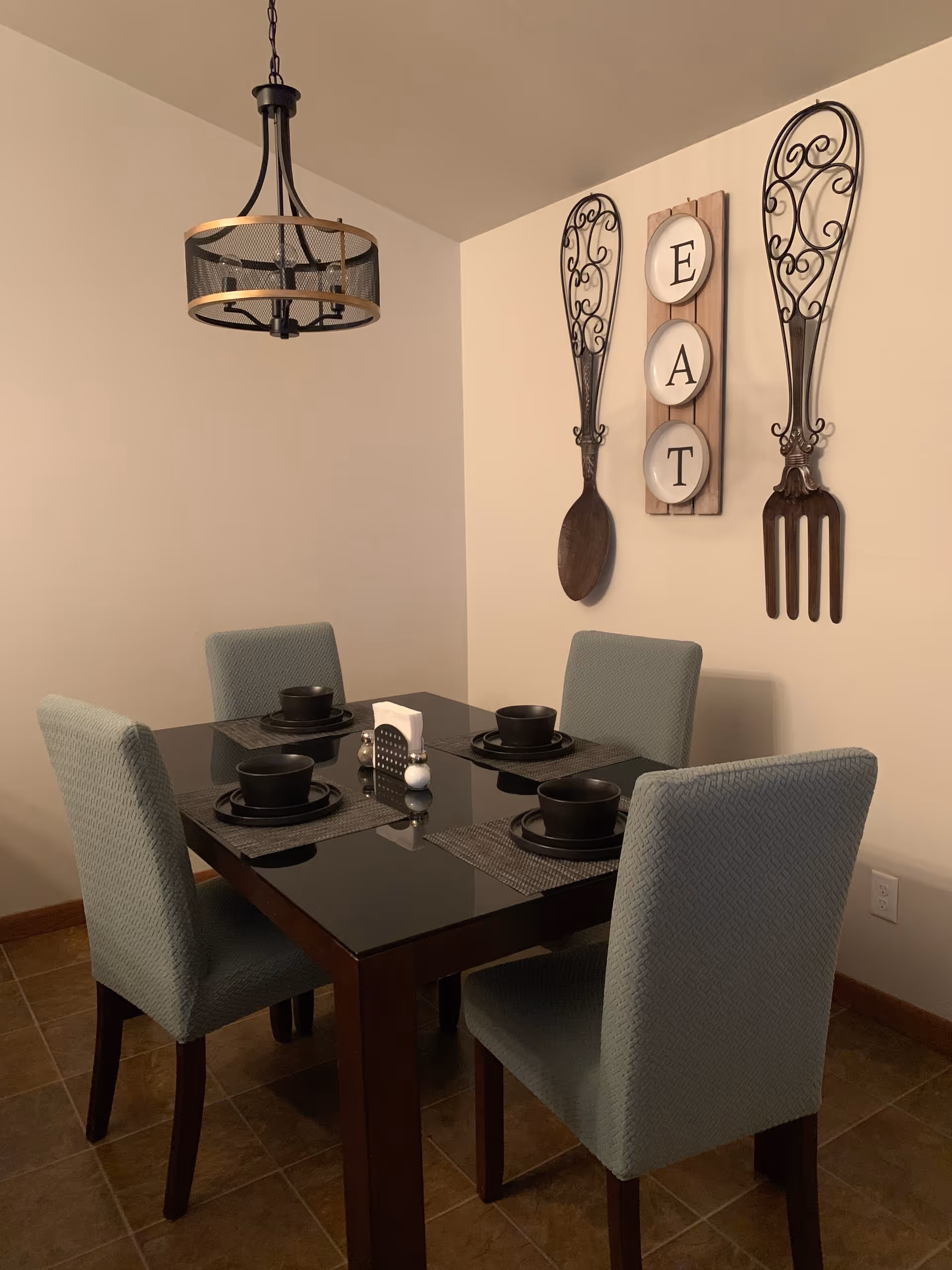 A small dining area with a dark table, four blue chairs, and decorative EAT wall art.