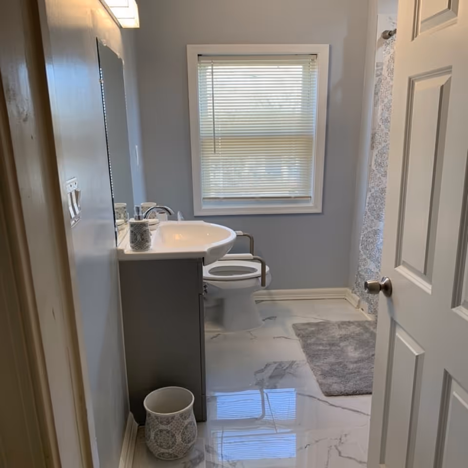 Small bathroom with sink, toilet, window blinds, and marble floor.
