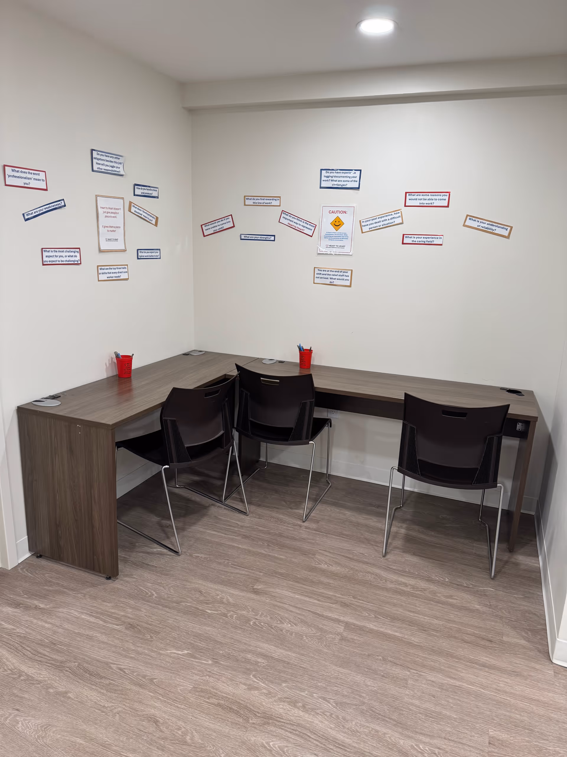 L-shaped wooden desk with four black chairs in a small conference corner covered with notes.
