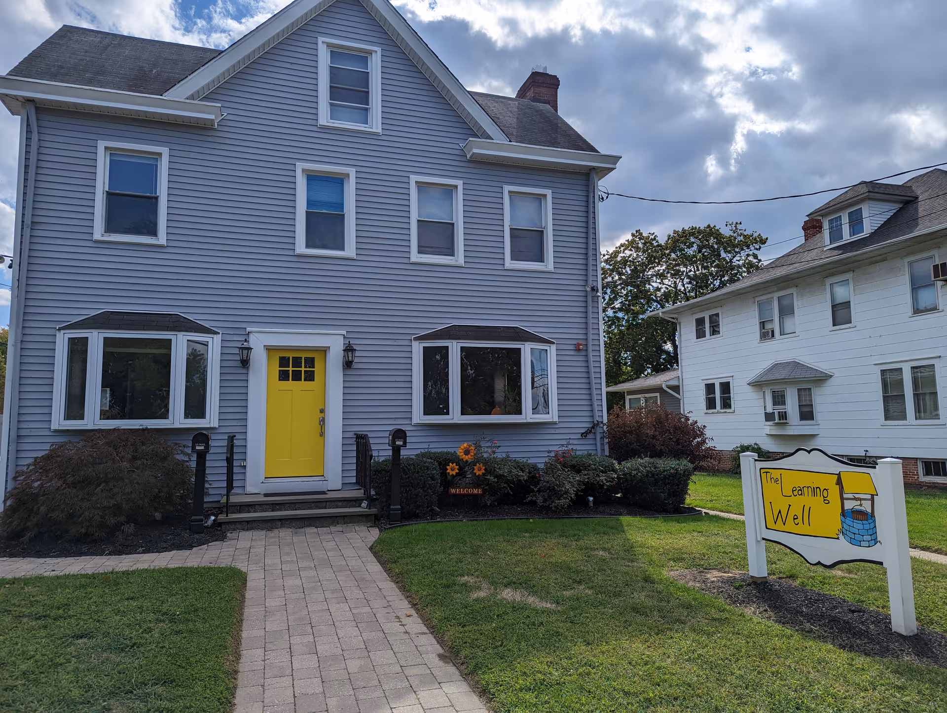 Two-story blue building with bright yellow door and a sign reading The Learning Well.