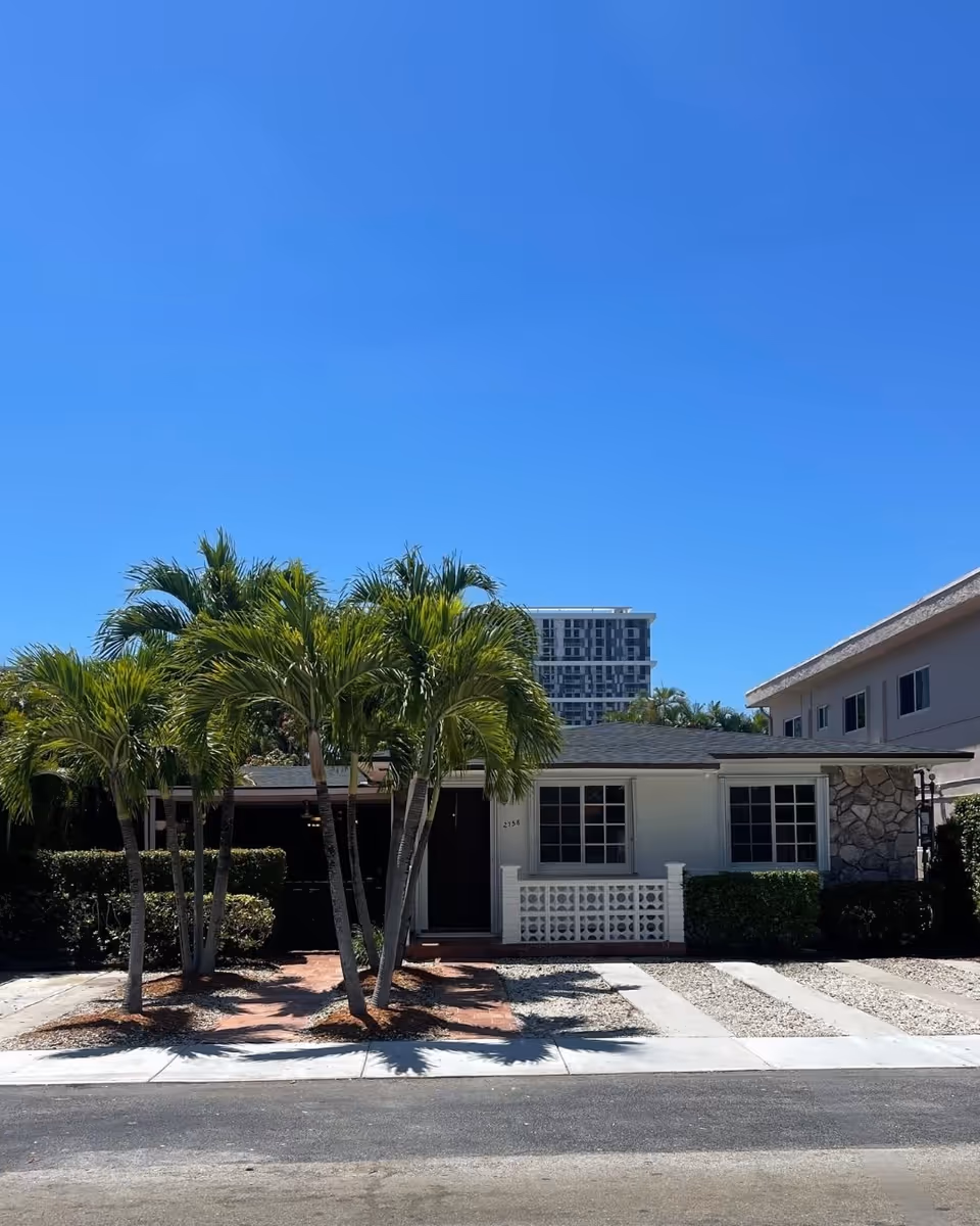 Single-story building front with palm trees and a driveway under a clear blue sky.