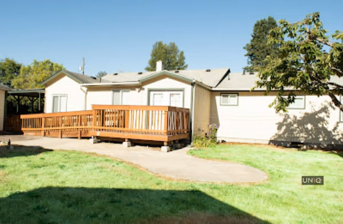 Single-story beige facility exterior with a wooden deck and green lawn under a blue sky.
