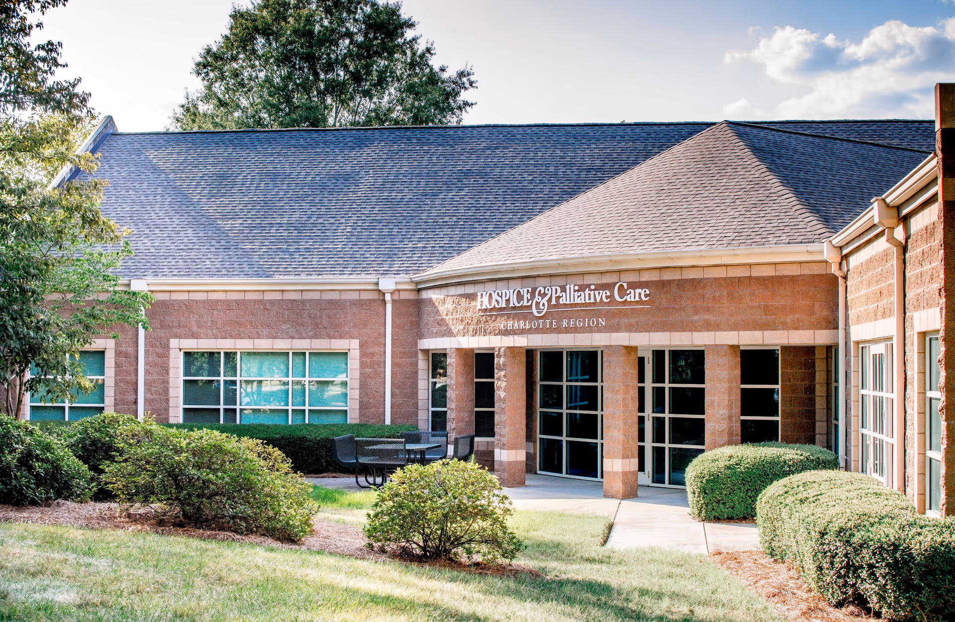 Exterior view of a brick hospice facility with glass entrance and manicured landscaping.