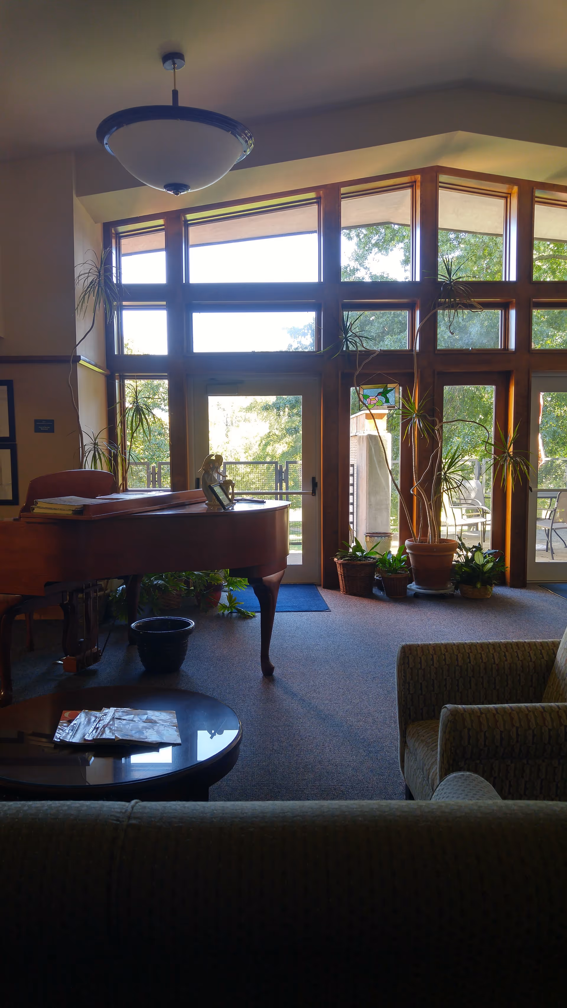 Sunlit lobby with piano, chairs, and large windows overlooking a patio.