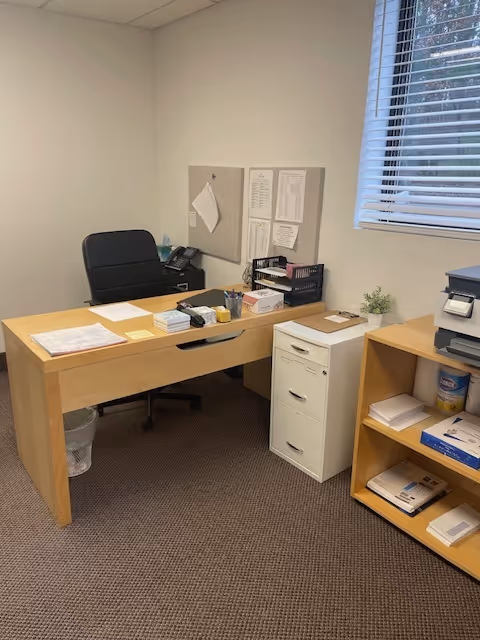 Tidy office area with wooden desk, chair, filing cabinet, shelves, and a window.