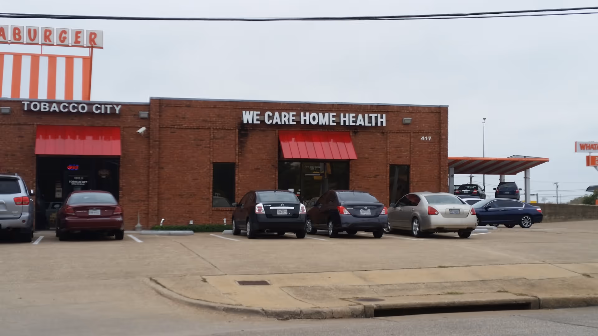 Exterior of a brick building with We Care Home Health sign and parked cars