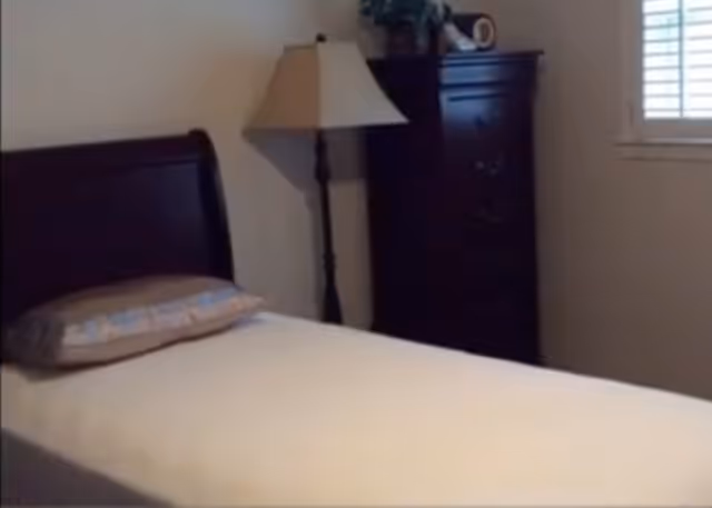 Bedroom with a single bed, lamp, tall dresser, and a window with blinds.