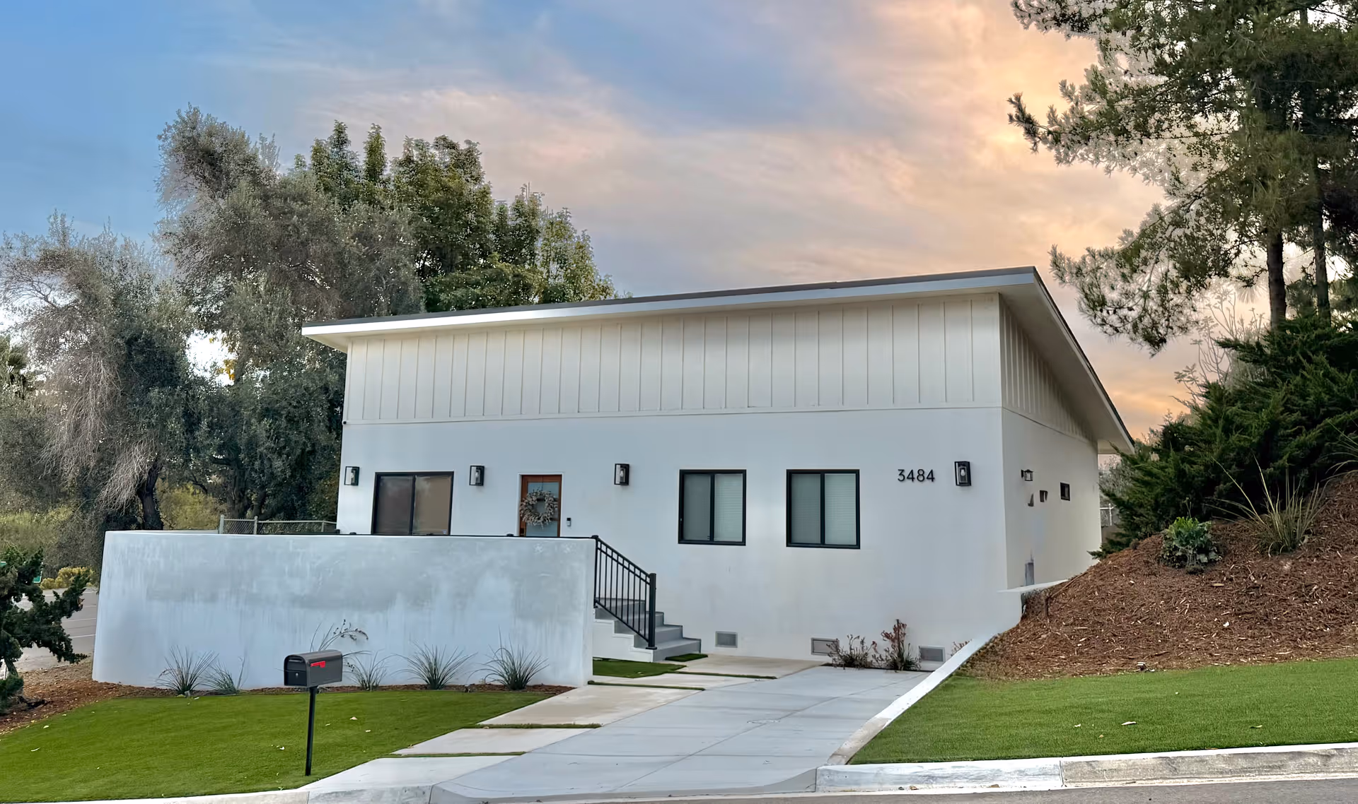 Modern white senior living building with front entrance, stairs, and landscaped lawn.