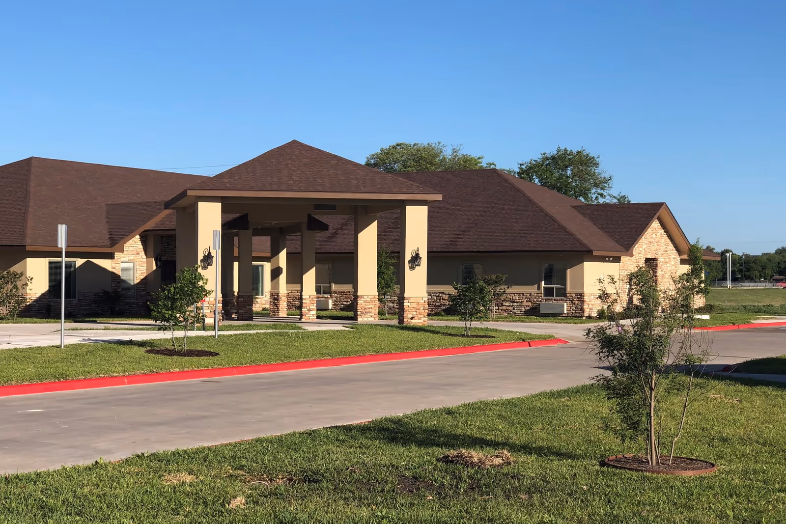 Low-rise senior living facility exterior with beige walls and a porte-cochere entrance.