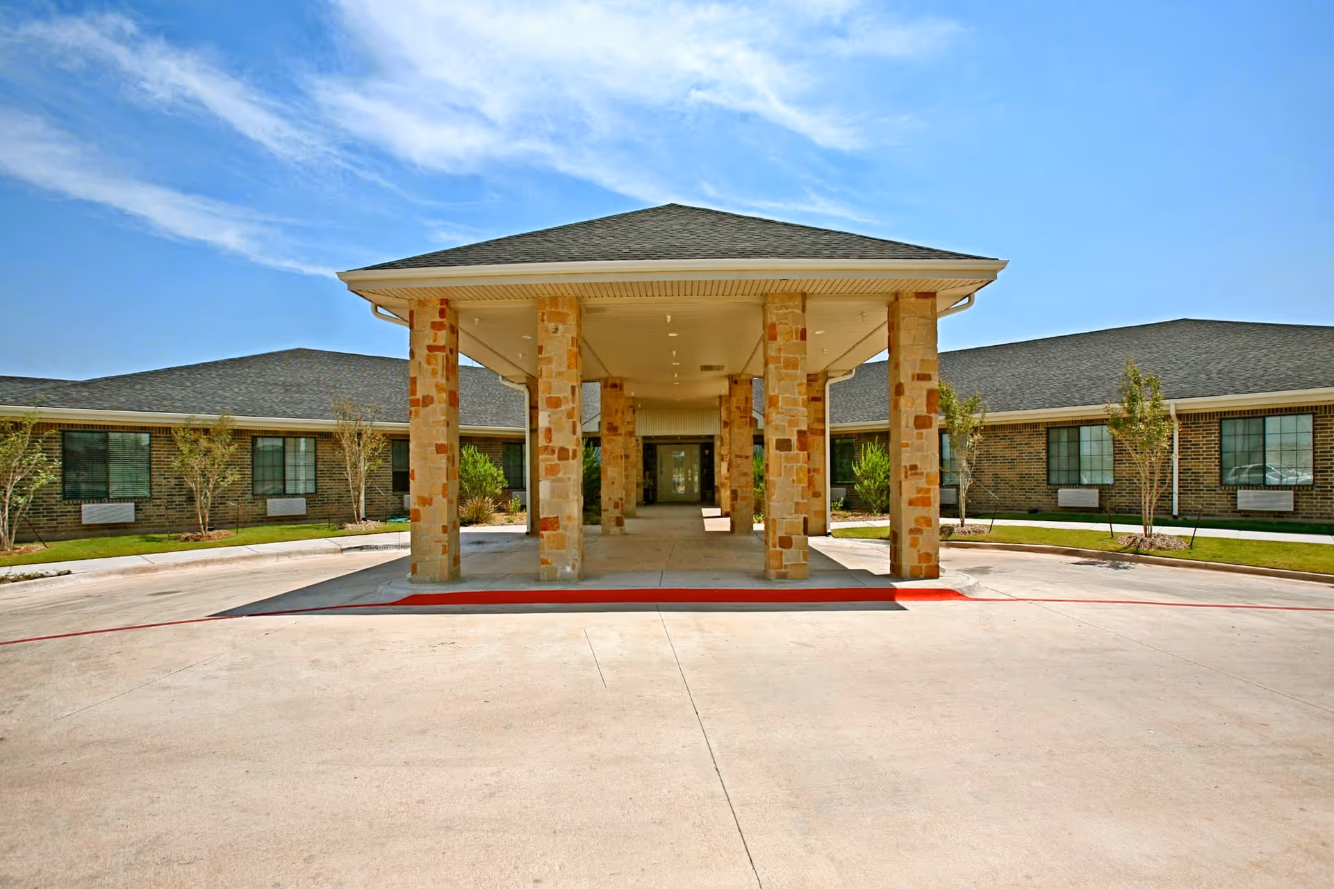 Front exterior of a senior living facility with a stone-columned entrance and covered driveway.