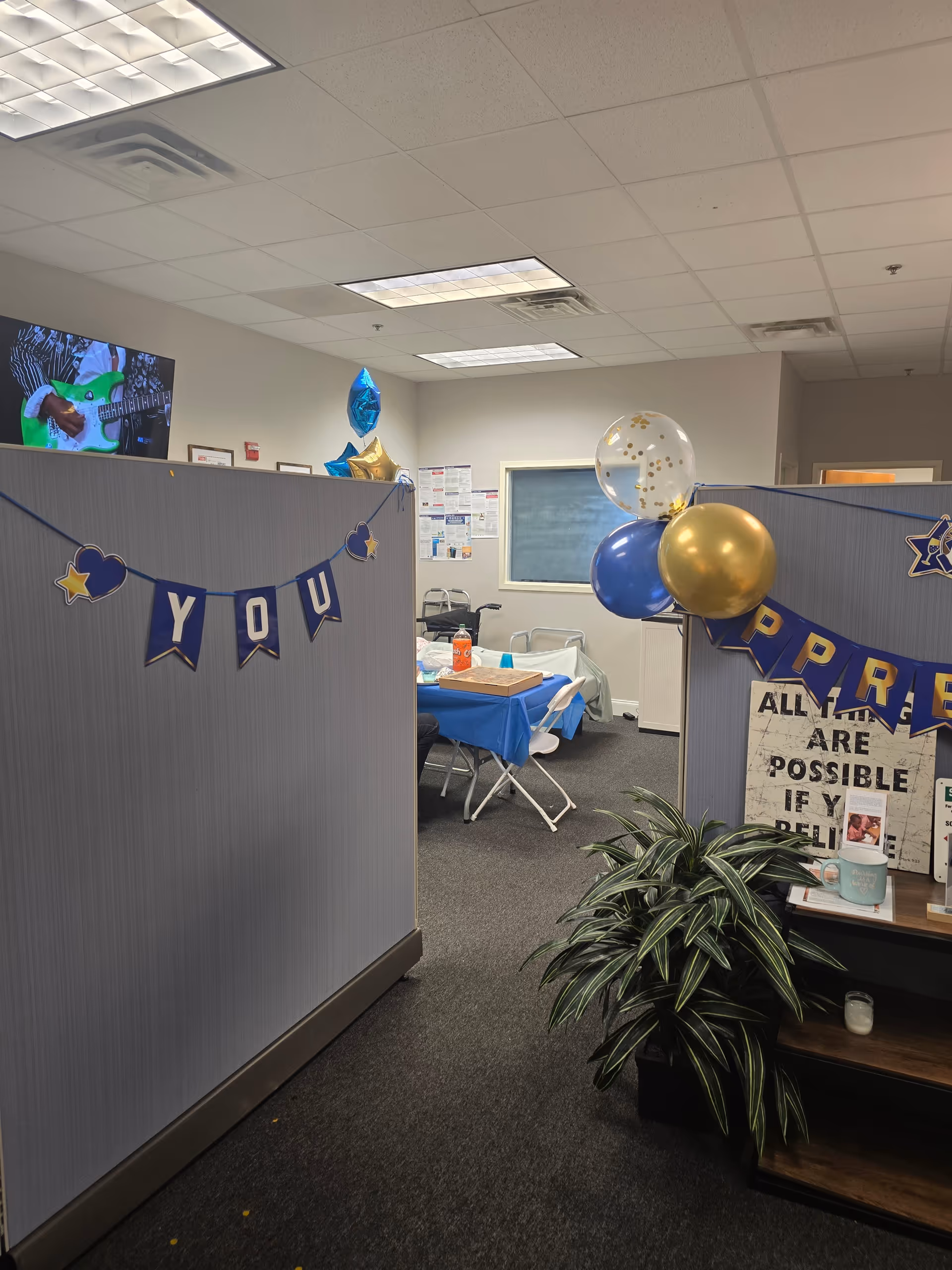 Indoor office-like space with cubicle dividers, balloons, and a decorated table for celebration.