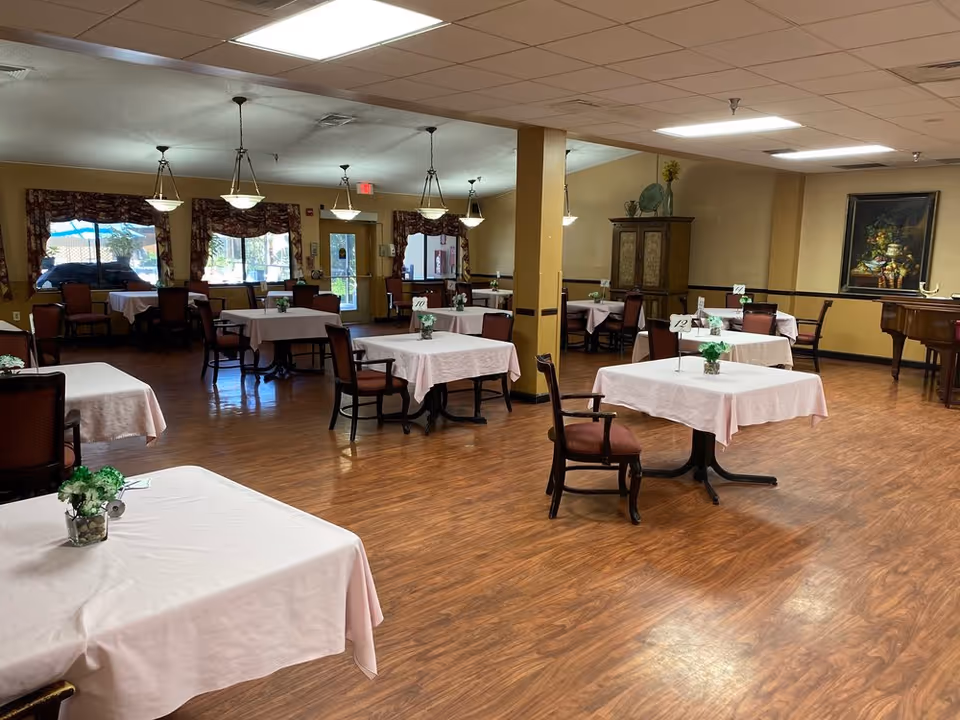 Spacious dining room with round tables, pink tablecloths, and burgundy chairs.