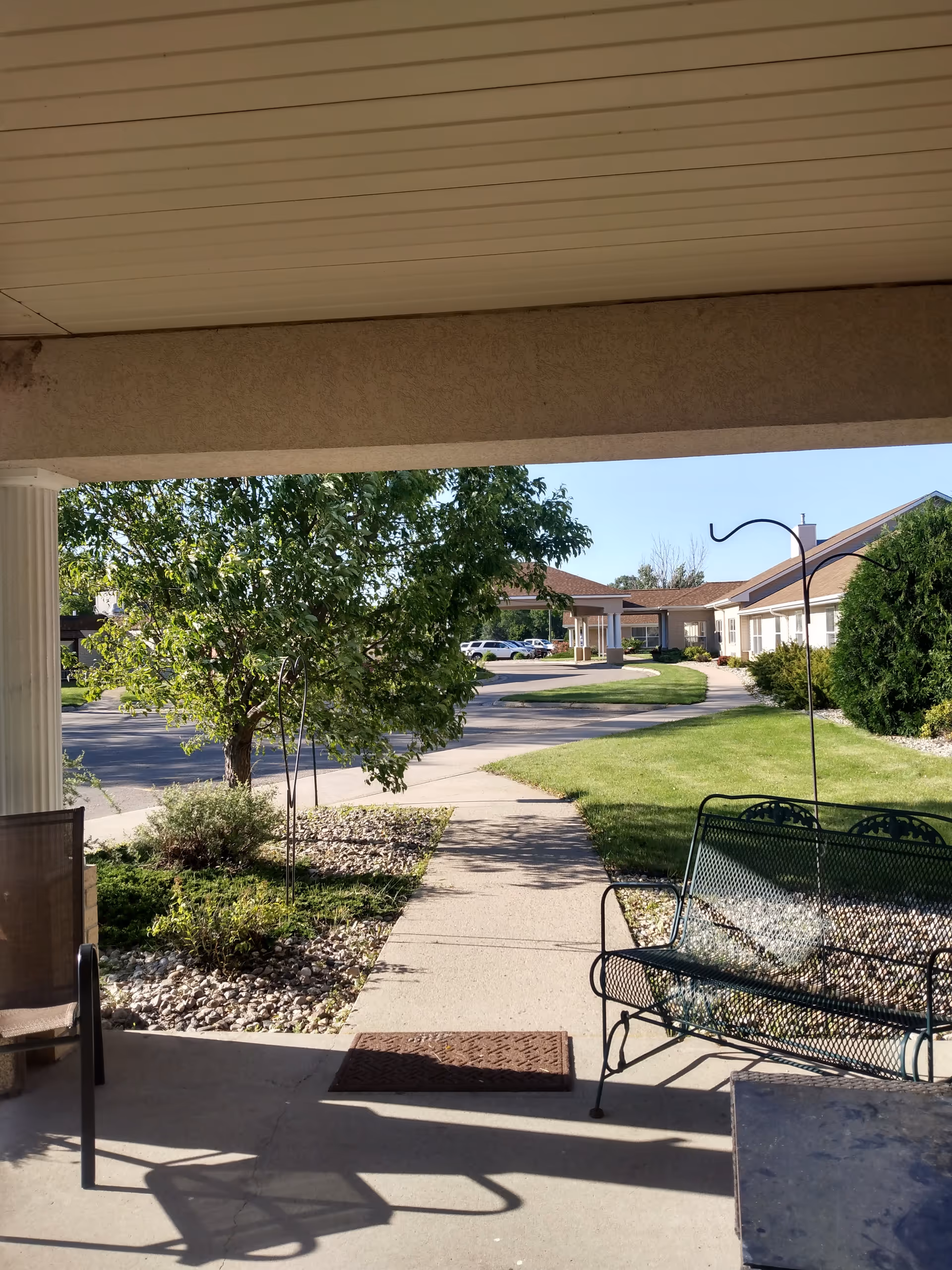 Covered patio overlooking a courtyard with benches, trees, and a sunny walkway.