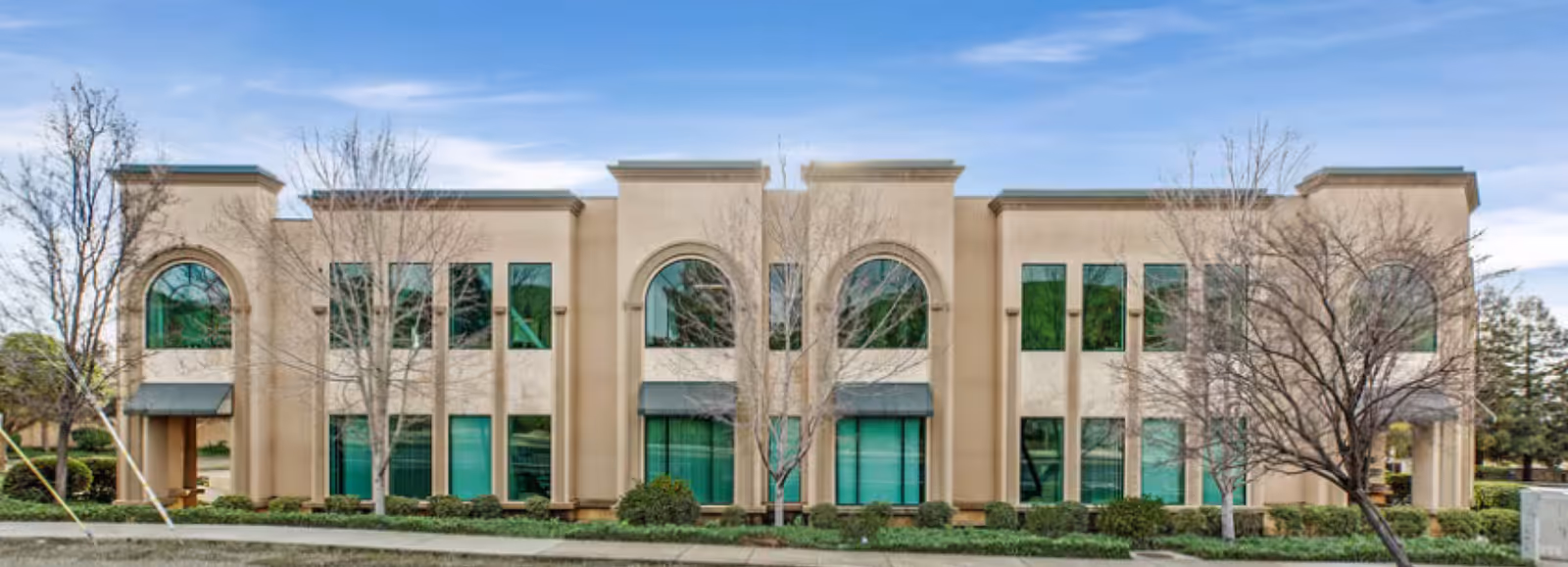 Beige, modern senior living facility facade with arched windows and a landscaped front.