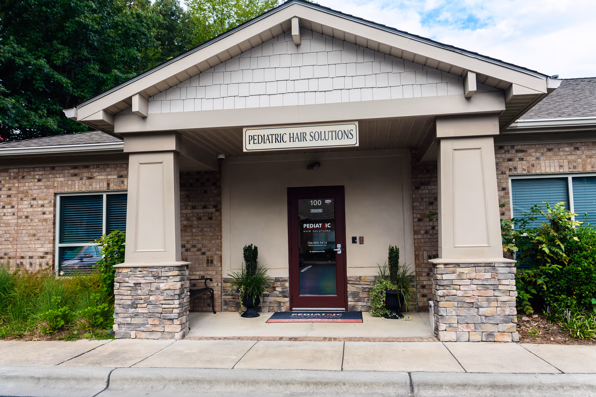 Front entrance of a brick building with a sign reading Pediatric Hair Solutions.