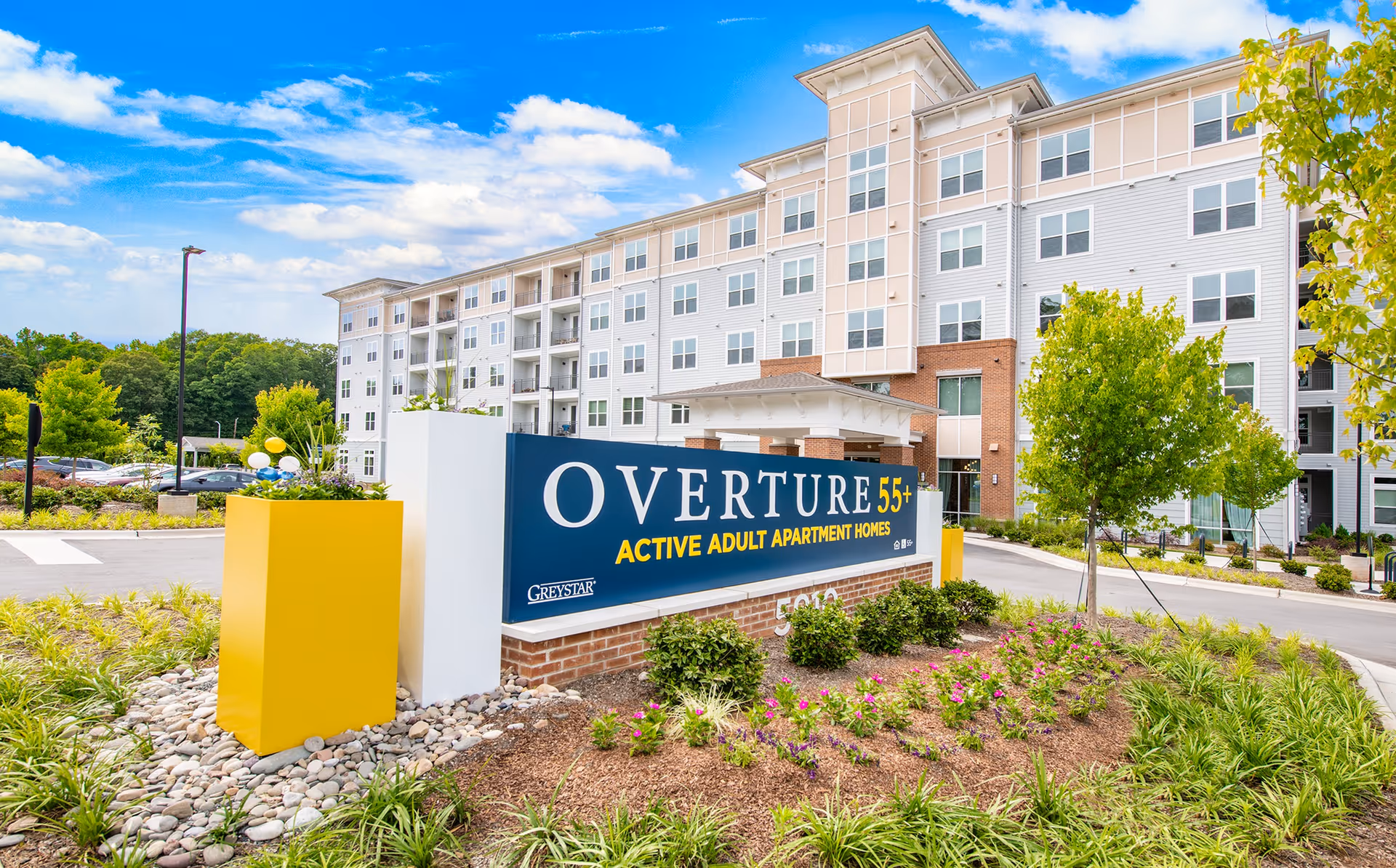 Entrance sign reading OVERTURE 55+ Active Adult Apartment Homes in front of a multi-story residential building with landscaped grounds.