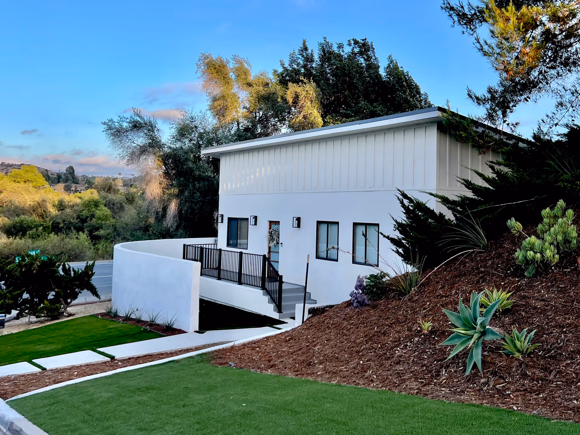 White modern facility exterior with stairs, railing, and landscaped hillside.
