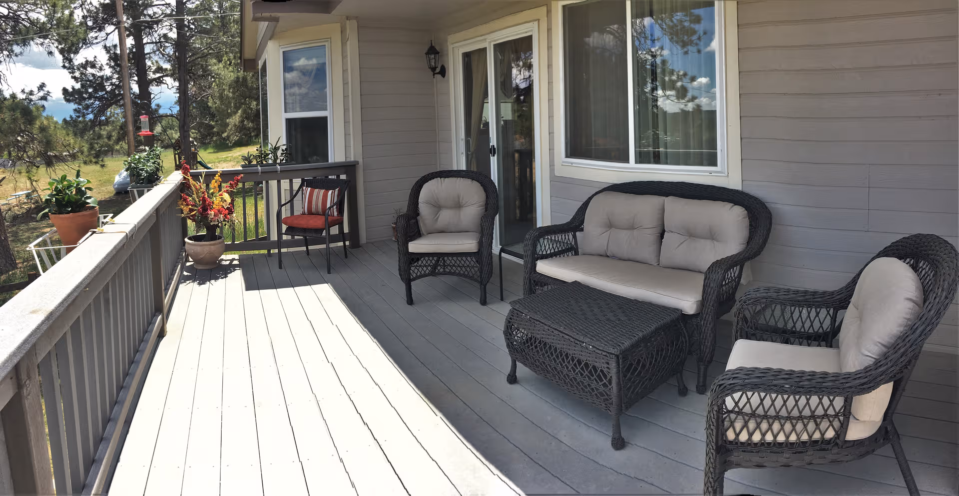 Outdoor deck with wicker seating and potted plants beside a residential home.