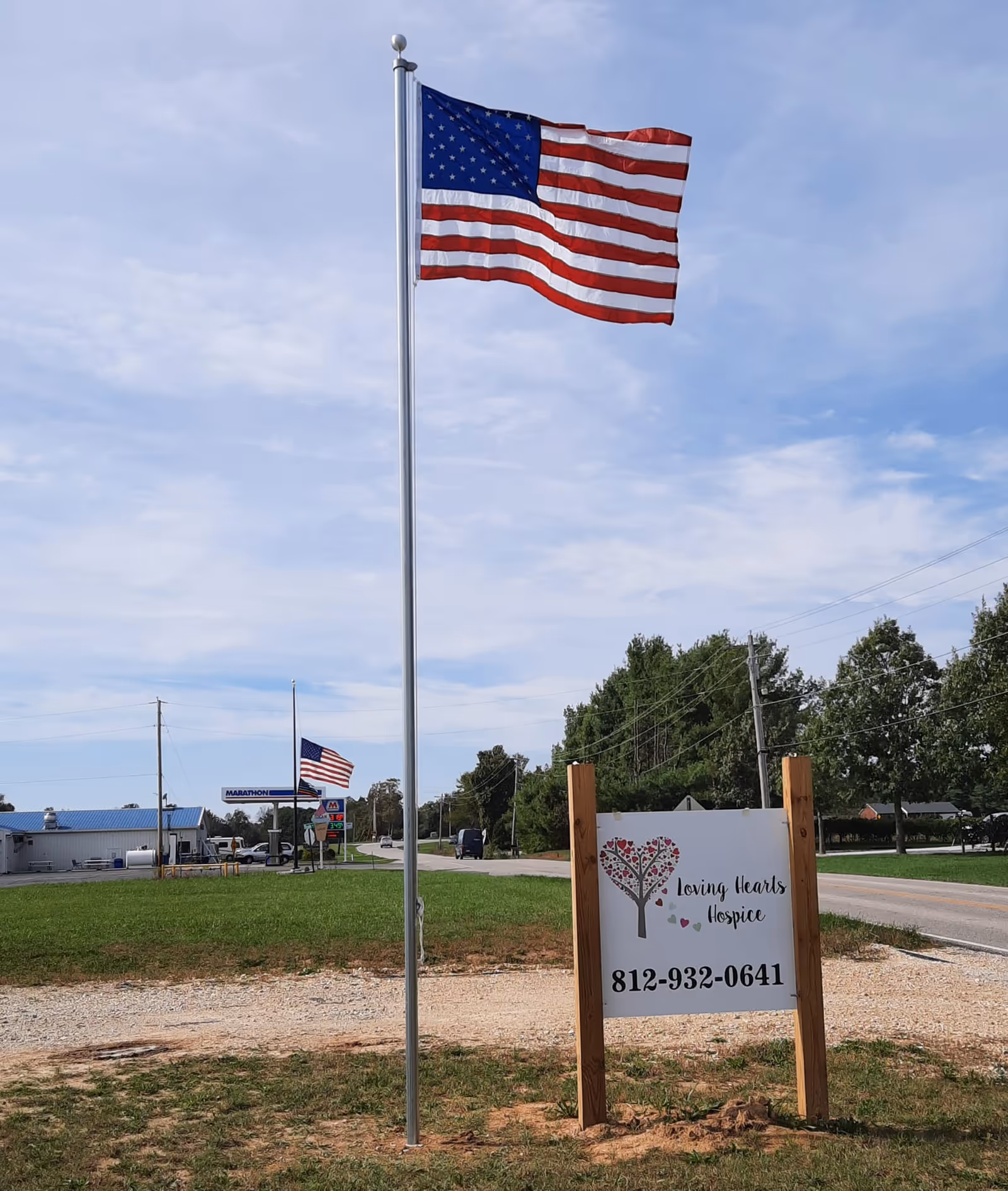 American flag on a tall pole beside Loving Hearts Hospice sign along rural road