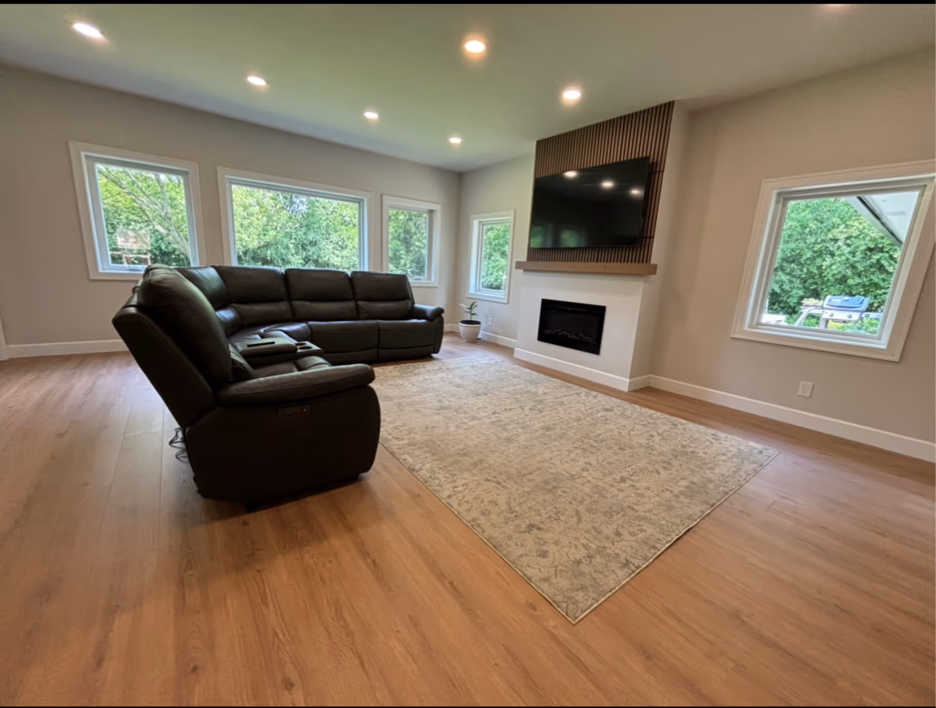 Bright modern living room in a senior facility with sectional sofa, rug, fireplace, TV, and windows.