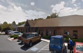 Single-story brick senior living facility with parked cars and a person near the entrance