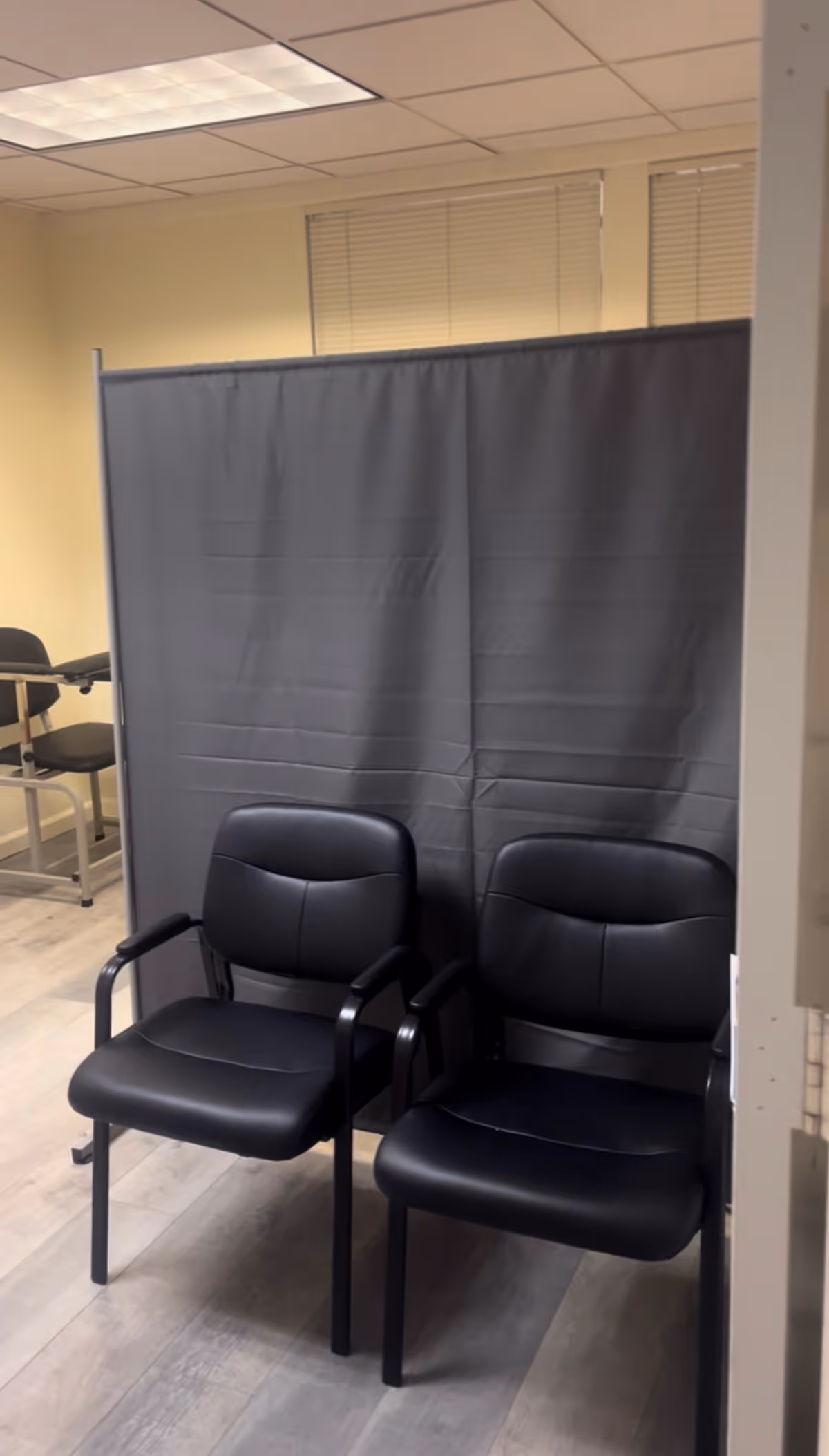 Two black chairs face a gray privacy curtain in a small interior waiting area.