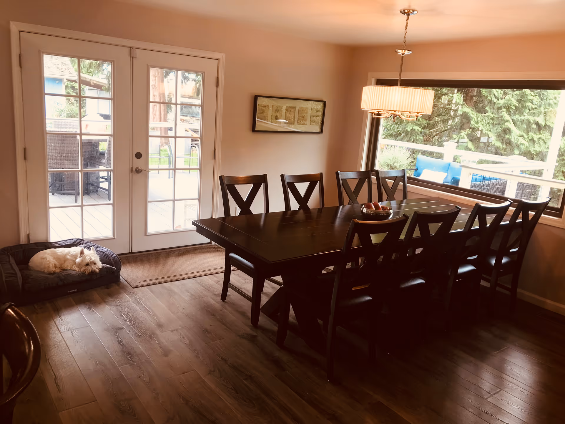 Sunlit dining room with a table, wooden chairs, French doors, and a dog bed in corner.