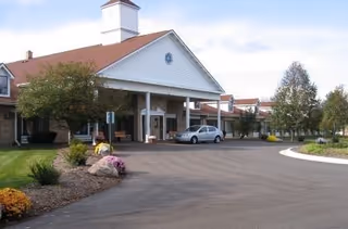 Exterior view of Delta Retirement Center showing the main entrance with a covered driveway, a parked car, landscaped greenery, and a clear sky.