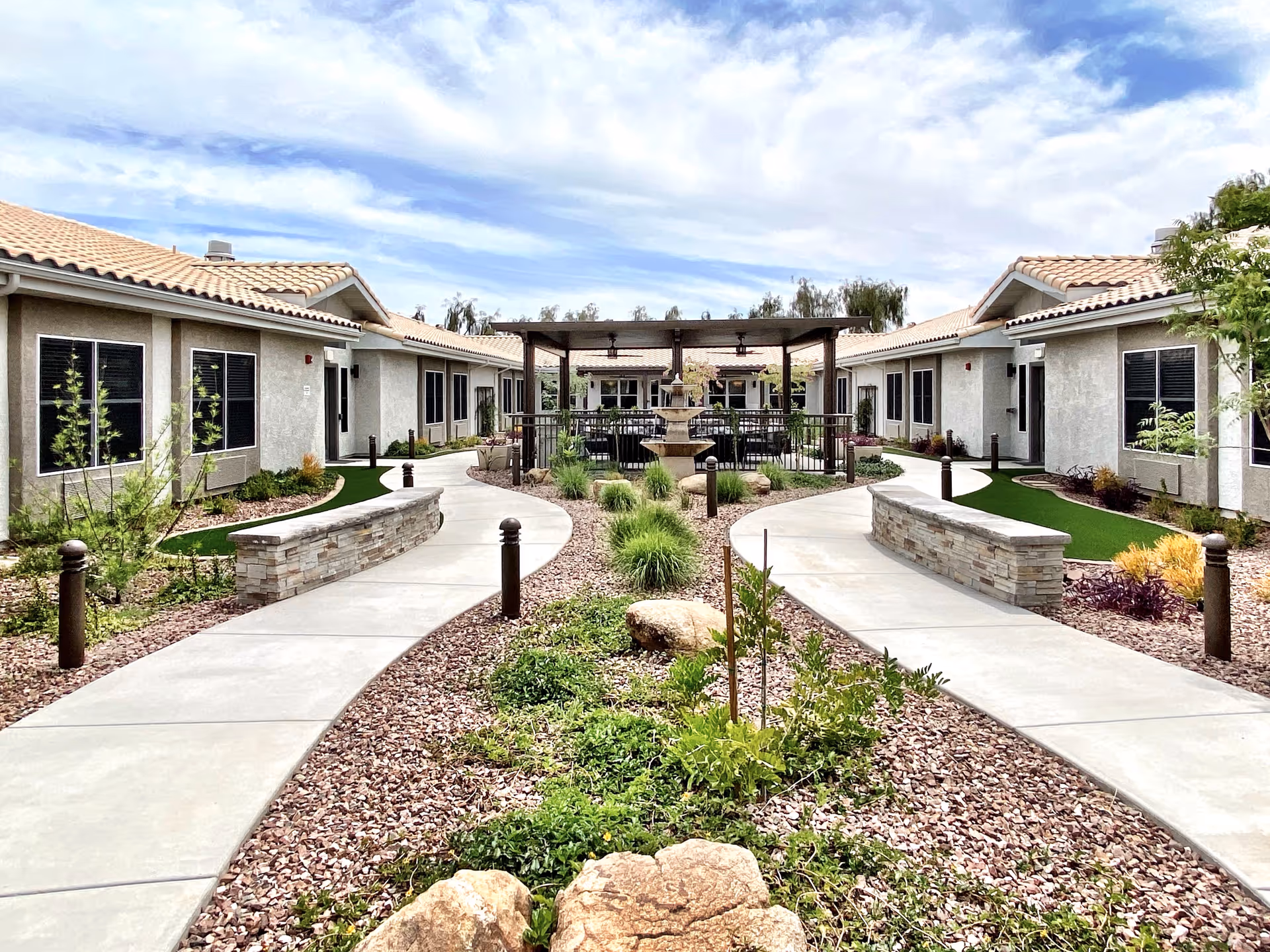 Landscaped central courtyard with curved walkways, a pergola and fountain flanked by single-story residential buildings.