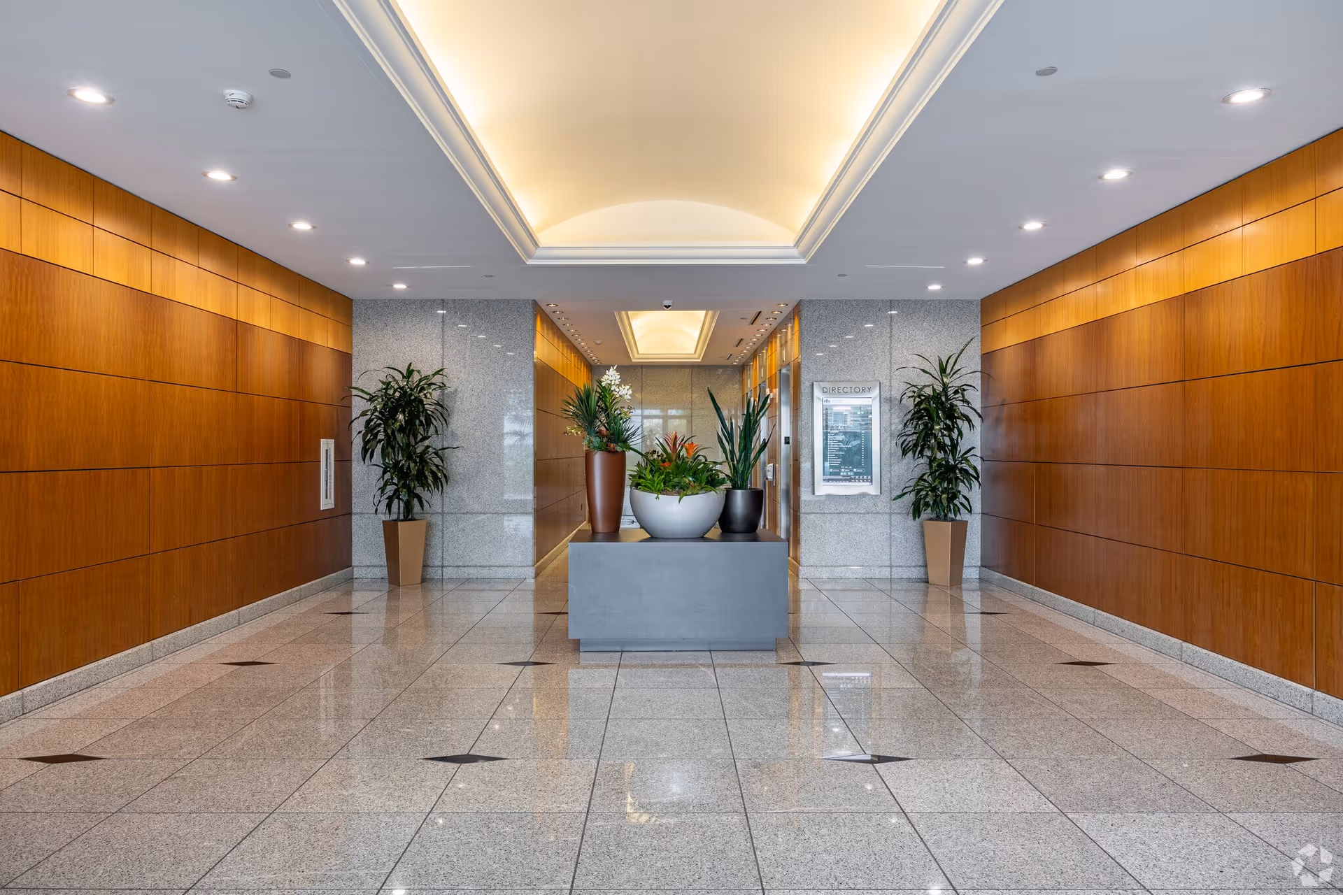 Bright lobby hallway of a senior living facility with wood-paneled walls and planters.