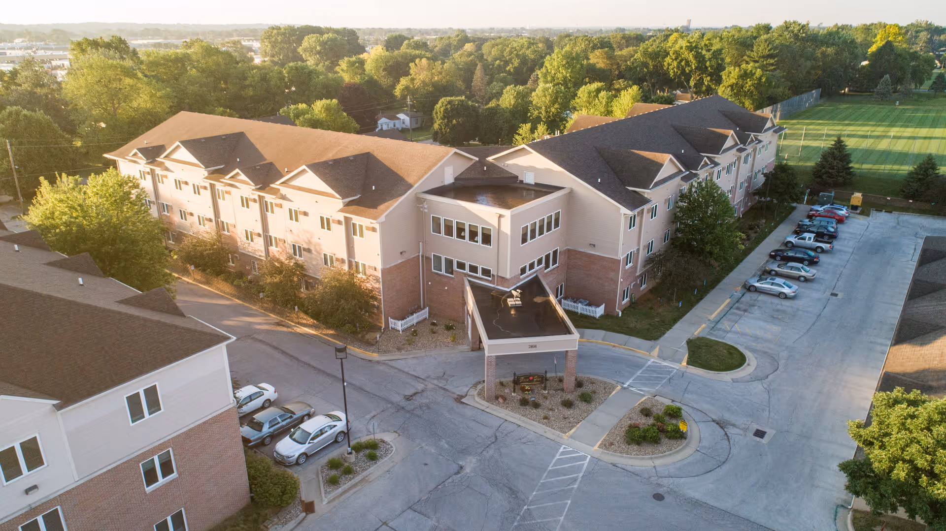 Aerial view of the Rose Glen senior living building with a covered entrance, parking lot, and surrounding trees.