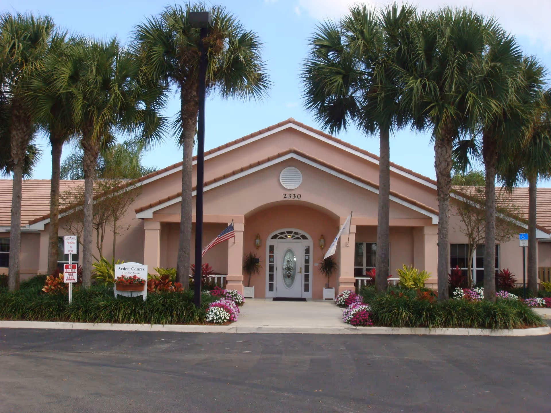 Front view of a pink senior living facility entrance with palm trees.