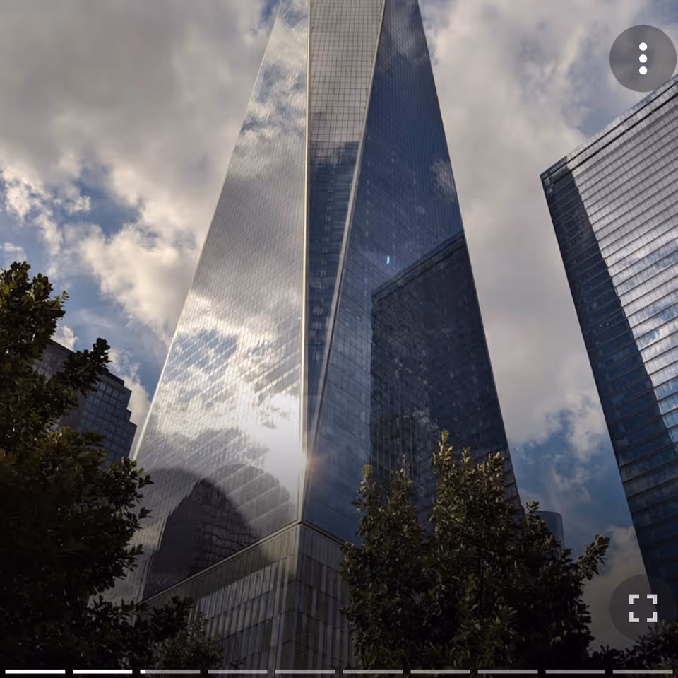 Tall glass skyscrapers reflect sunlight against a cloudy sky, with trees in foreground.