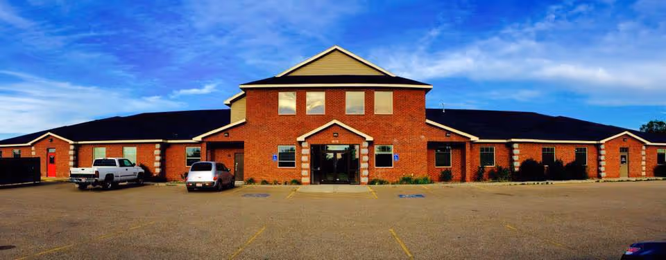 Brick building with central entrance and parking lot, front view of senior care facility.
