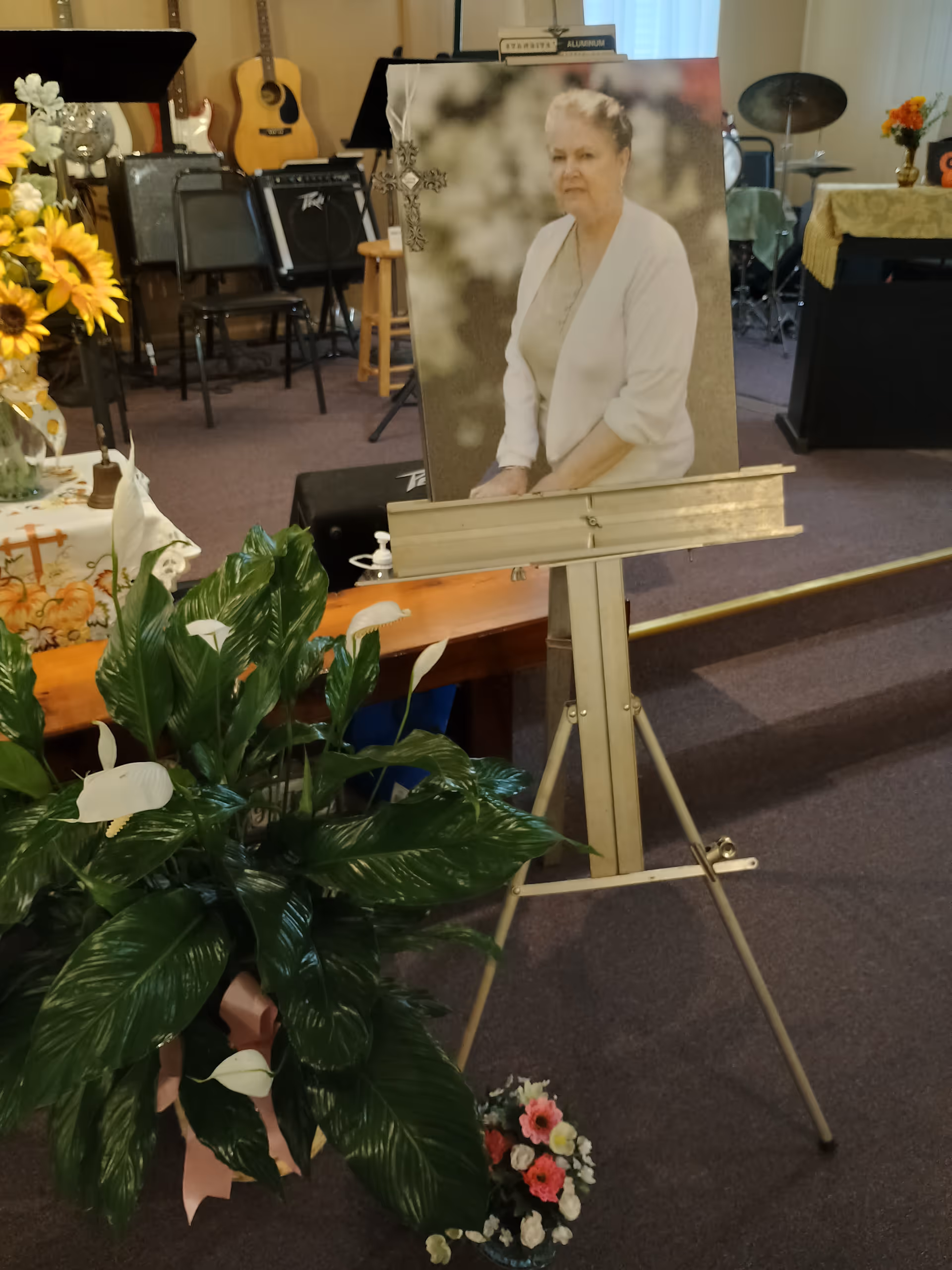 Interior room with memorial portrait on easel, flowers, and a music setup in back.
