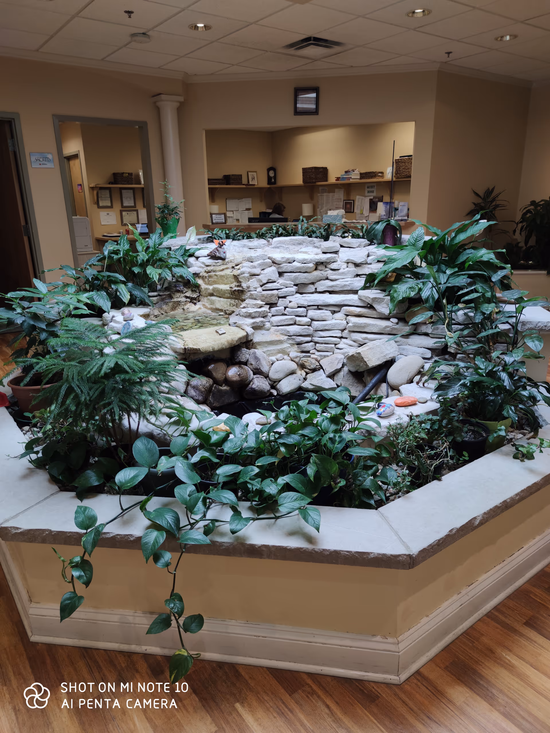 Indoor lobby features a stone fountain surrounded by greenery in a reception area.