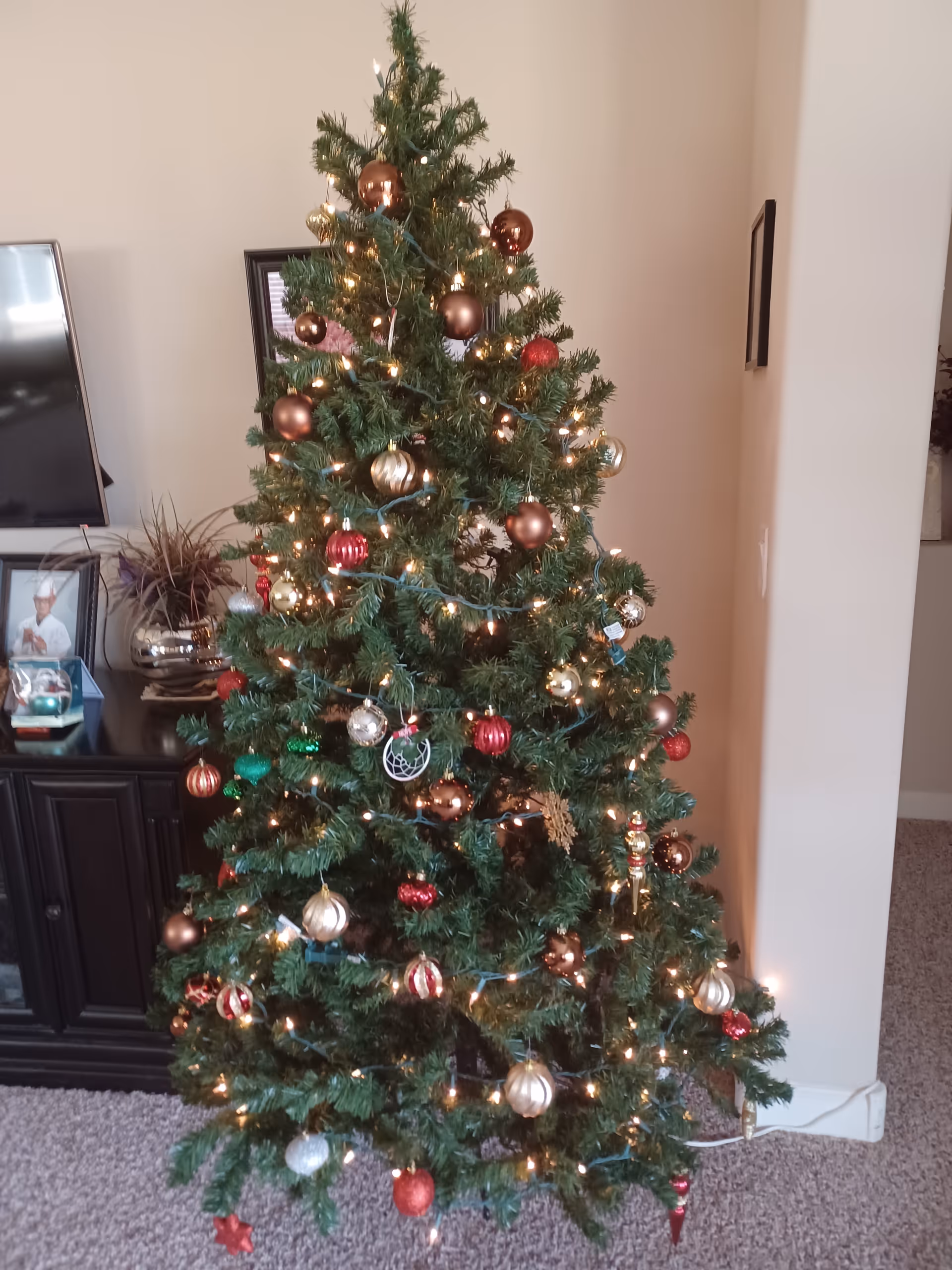 A decorated Christmas tree with lights stands in a living room beside a cabinet.