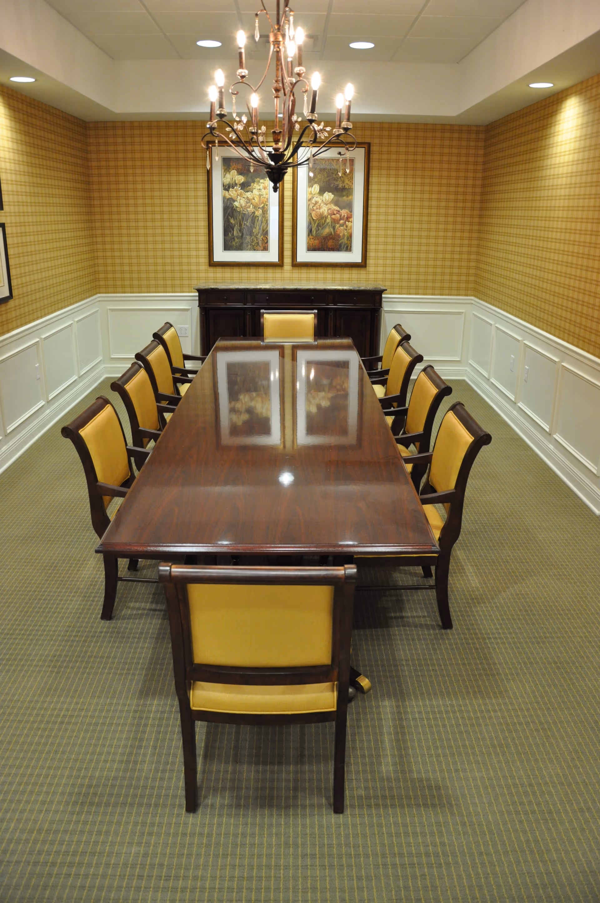 Long wooden dining table with yellow chairs in a formal, paneled dining room.