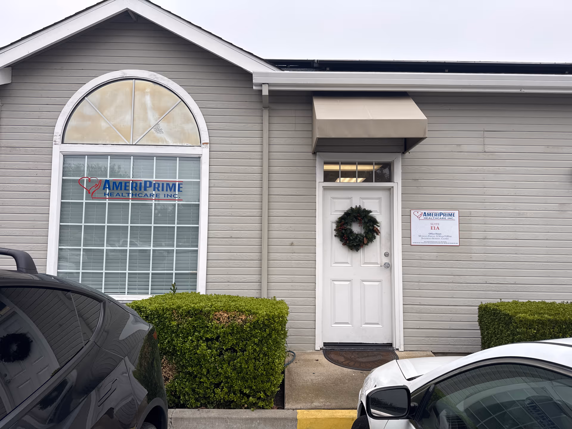 Exterior view of AmeriPrime Healthcare Inc. building entrance with wreath and parked cars.