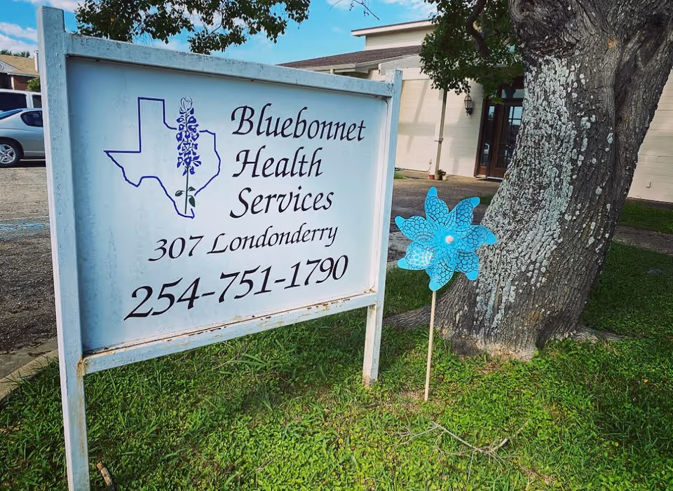 Bluebonnet Health Services hospice sign outside with a tree and building in background