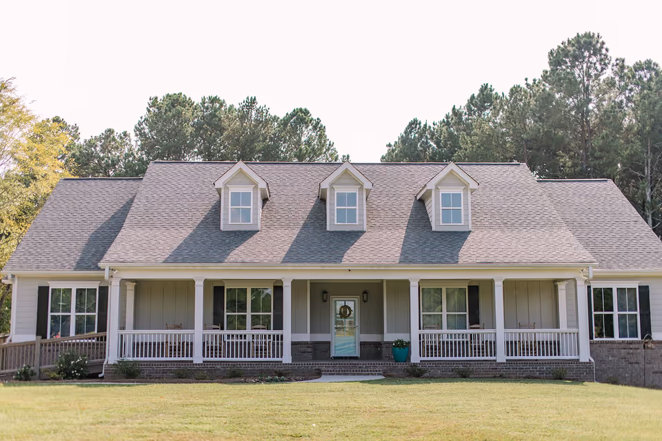 A large house-style senior living facility with a wraparound front porch and manicured lawn