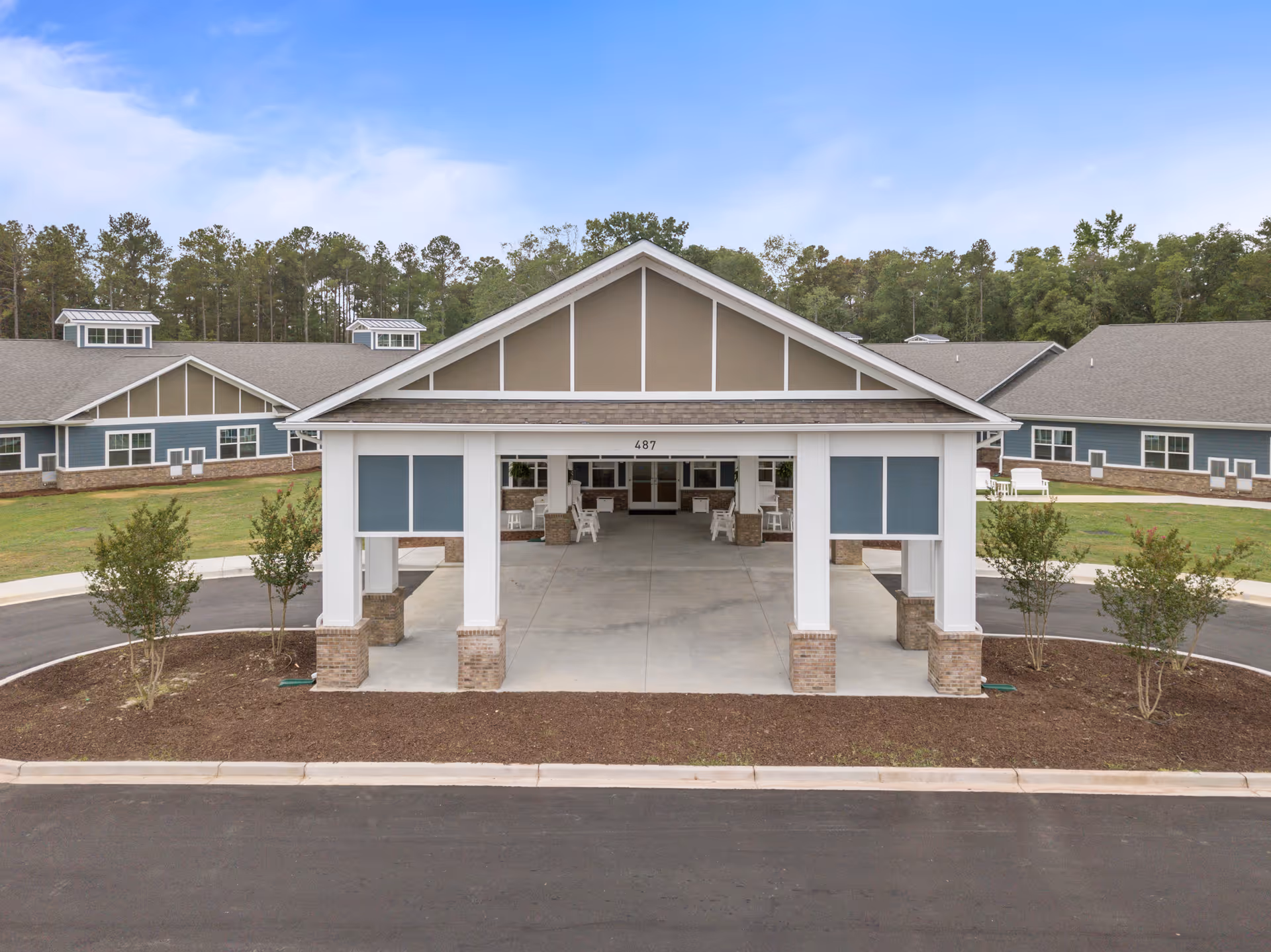 Covered entrance porte-cochere of a single-story senior living building with columns, driveway, and surrounding landscaping.