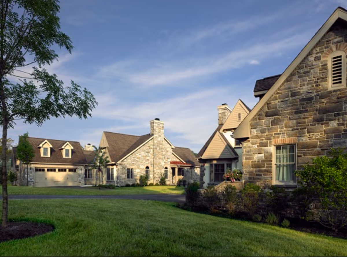 Stone-faced residential buildings with a manicured lawn, trees, and a blue sky.