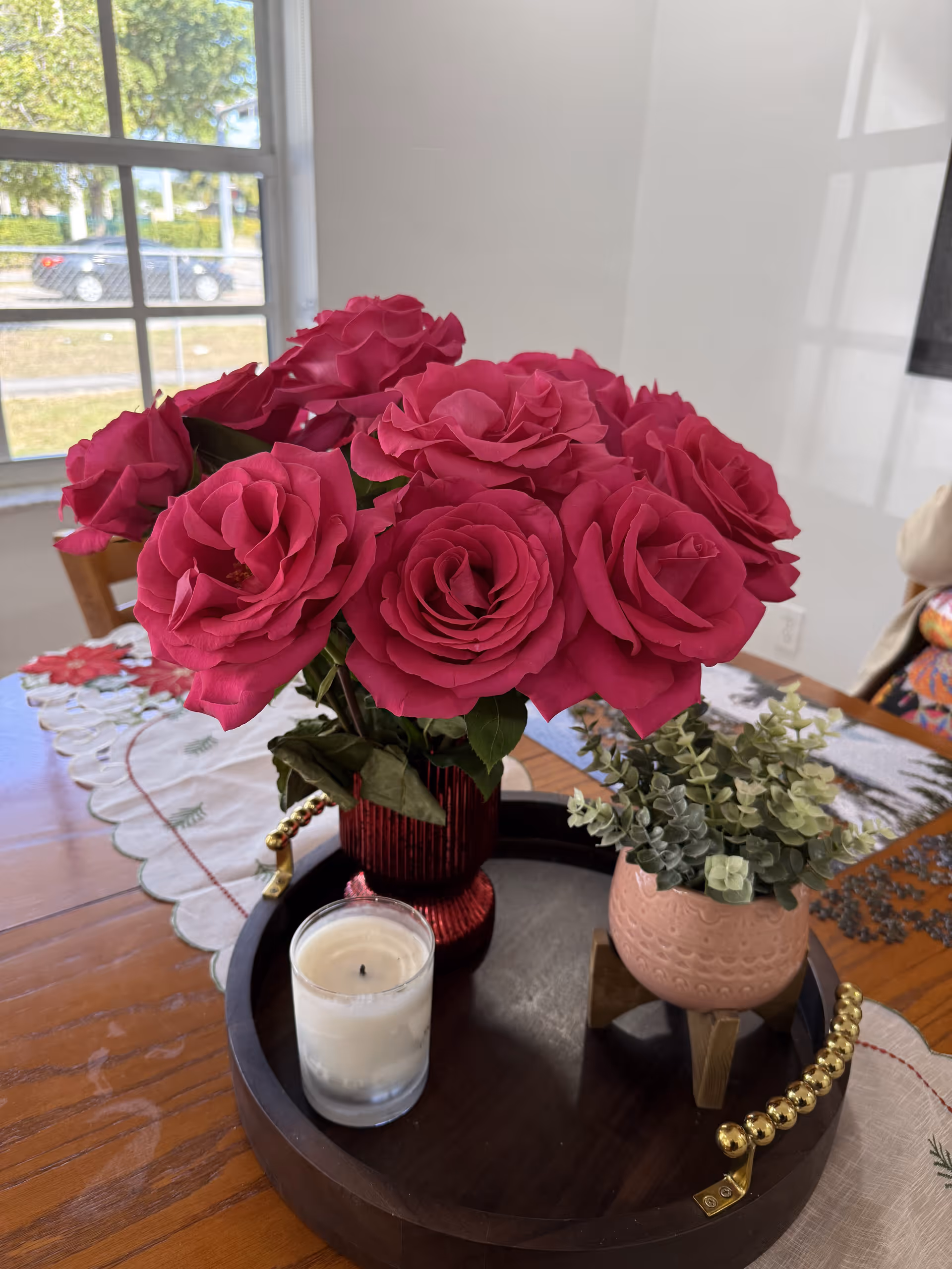 Tabletop centerpiece of pink roses with candle and succulents on a dining table.