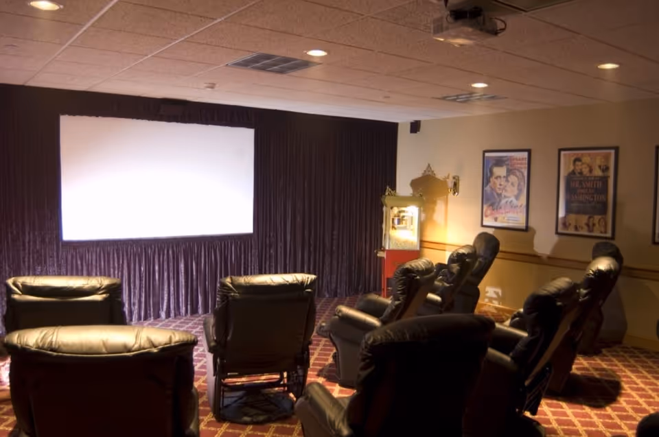 Small screening room with several leather recliner seats facing a blank projection screen and a popcorn machine.