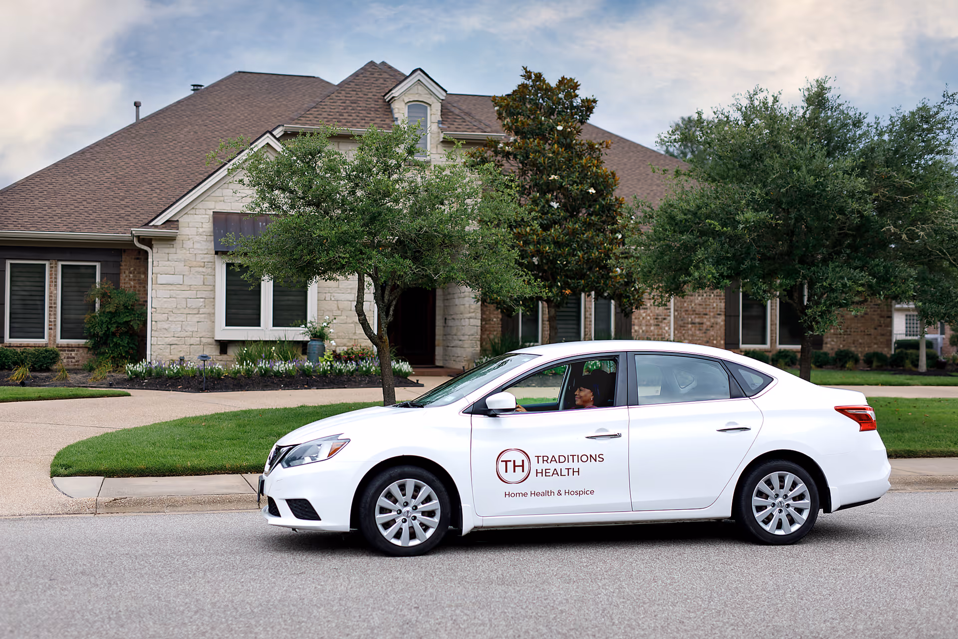 White Traditions Health car parked in front of a brick senior living facility with trees.