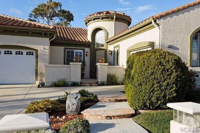 Front exterior of a single-story Mediterranean-style residence with a tiled roof, arched entry tower, garage, and landscaped walkway.