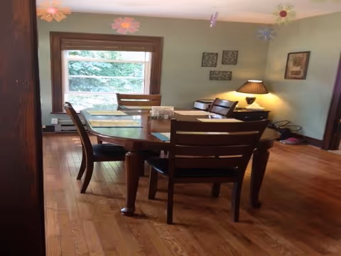 Wooden dining table with chairs in a bright room with a window and hanging flower decorations.