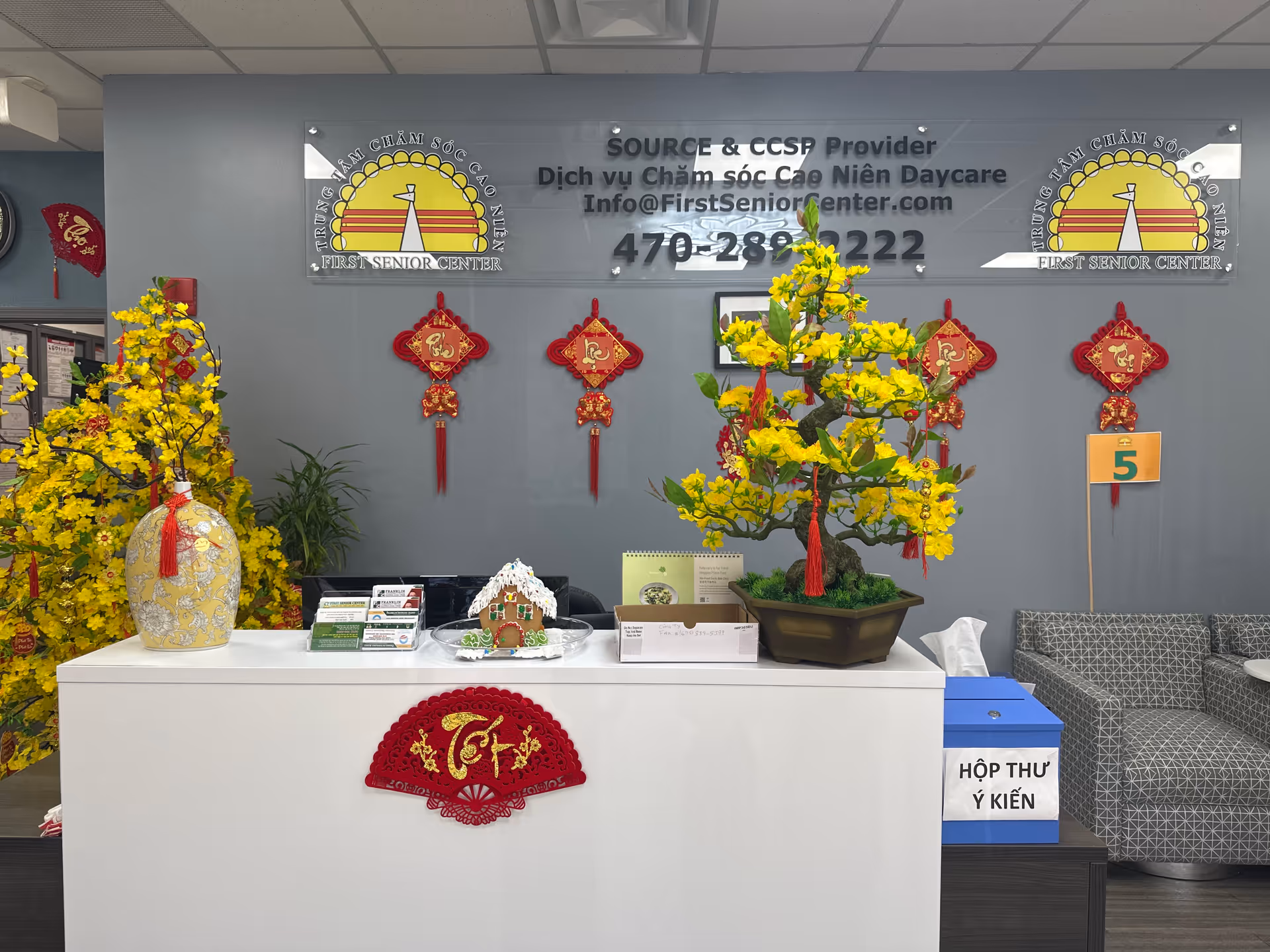 Reception desk in a senior center lobby with yellow flowering plants and red decorations.